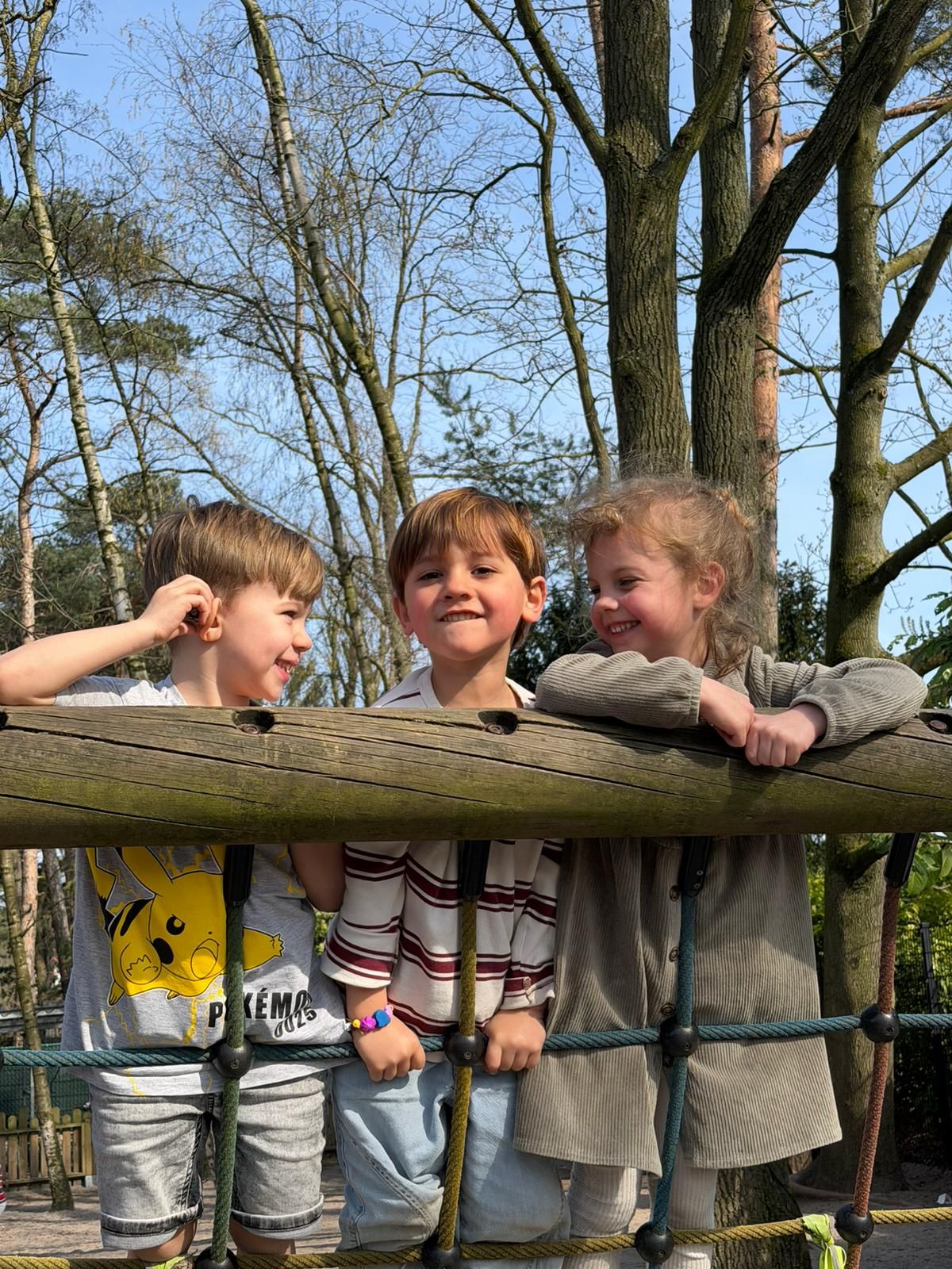 Drie kinderen leunen op een houten hek tussen de bomen